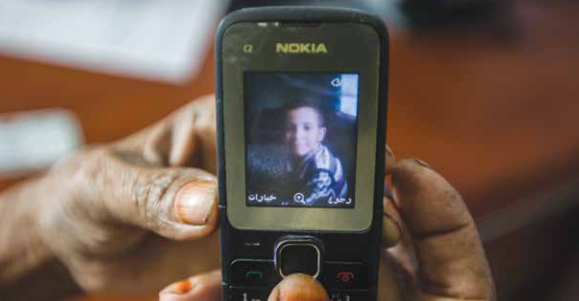 Yemeni refugee shows his son's picture on a mobile phone